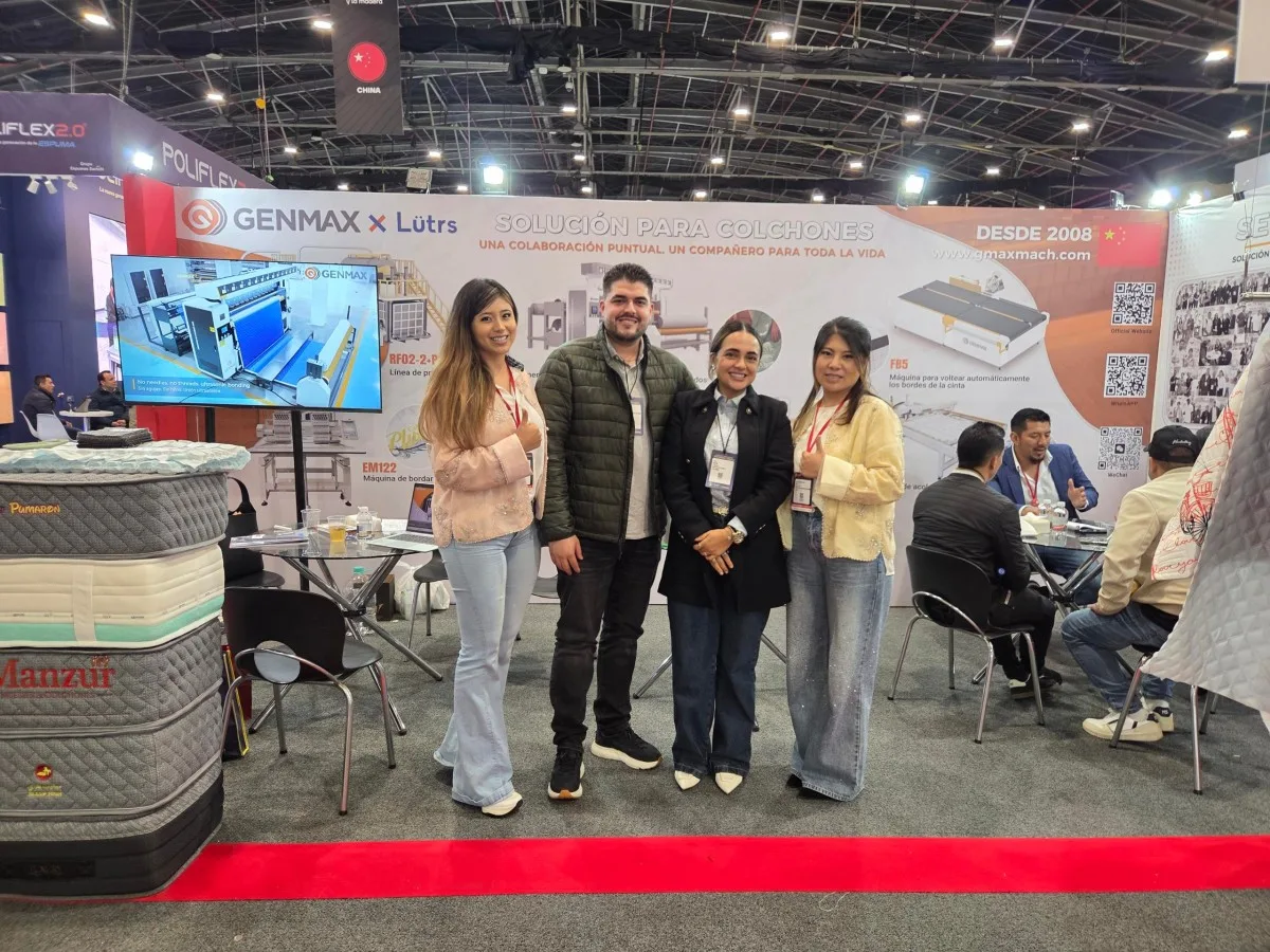 GENMAX sales representative posing with three industry visitors in front of the GENMAX x Lütrs "Solución Para Colchones" booth backdrop at Interzum Bogotá 2026
