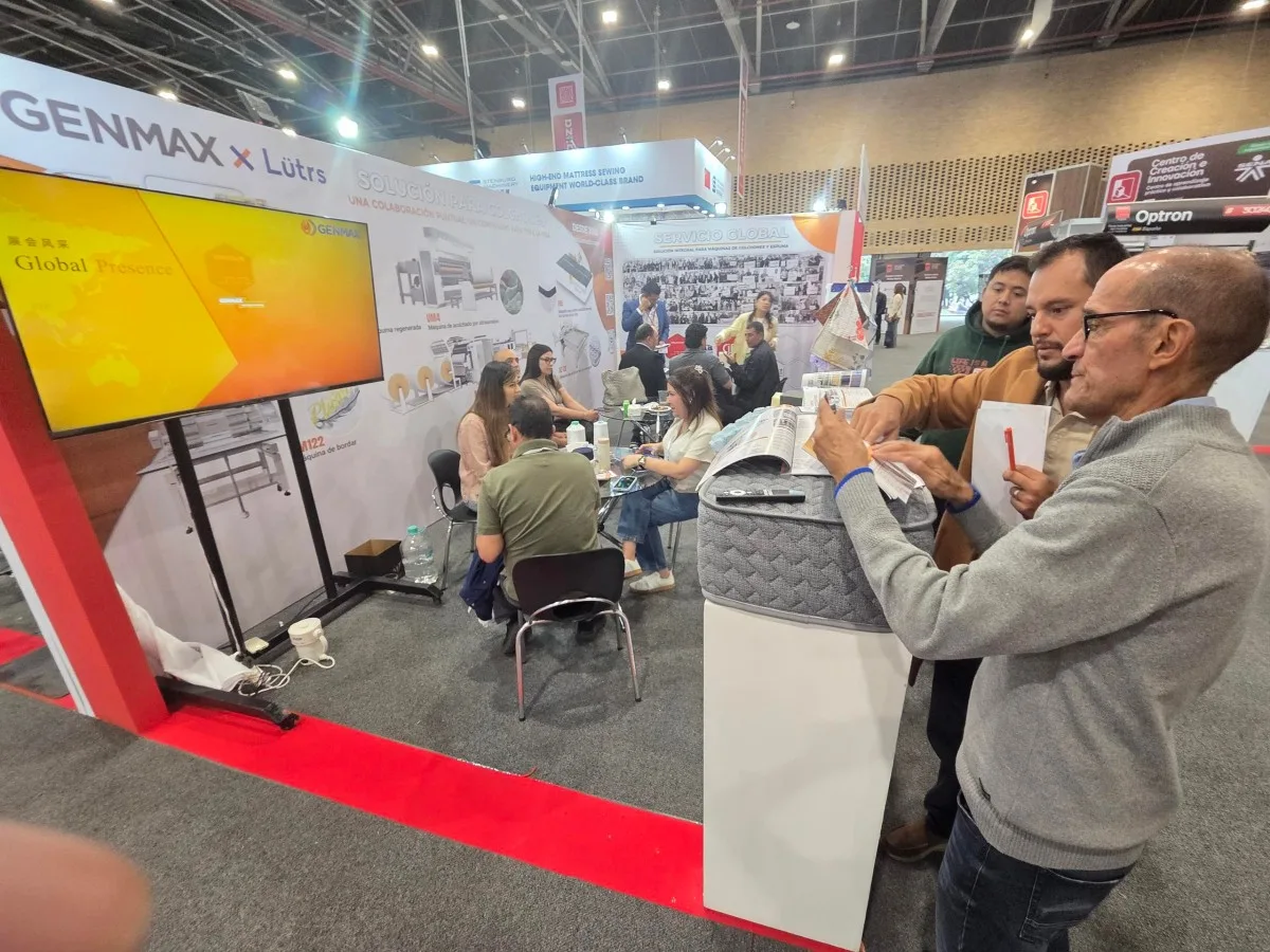 GENMAX representative demonstrating mattress spring and foam material samples to a group of interested visitors at the GENMAX booth, Interzum Bogotá 2026, Corferias, Colombia
