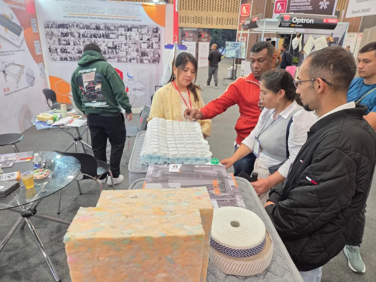 Wide view of the busy GENMAX x Lütrs booth at Interzum Bogotá 2026, showing multiple simultaneous client consultations in progress, with the GENMAX product presentation screen displaying "Global Presence"